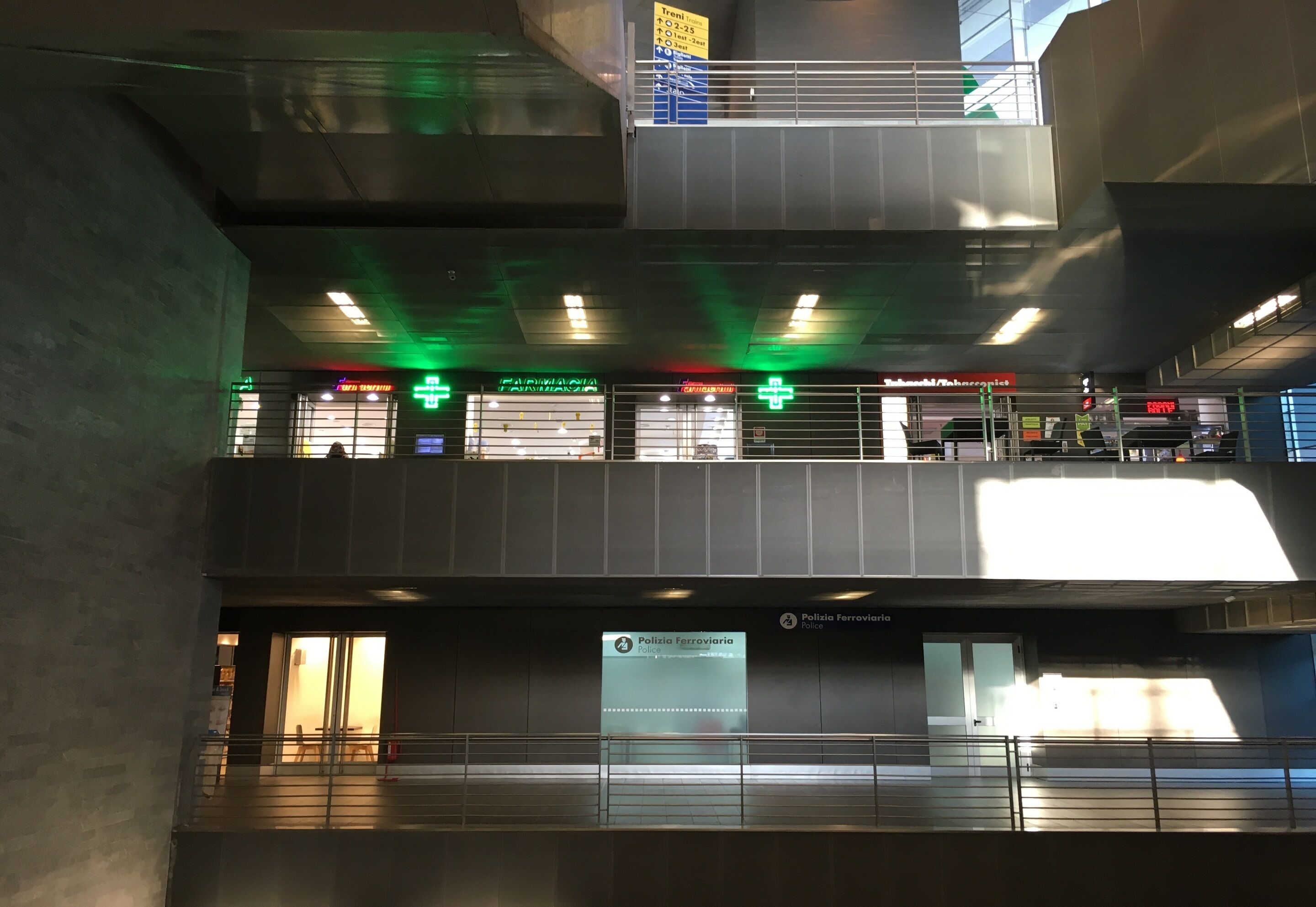 A multi-level indoor space with a sign for 'Polizia Ferroviaria Police' and a pharmacy.