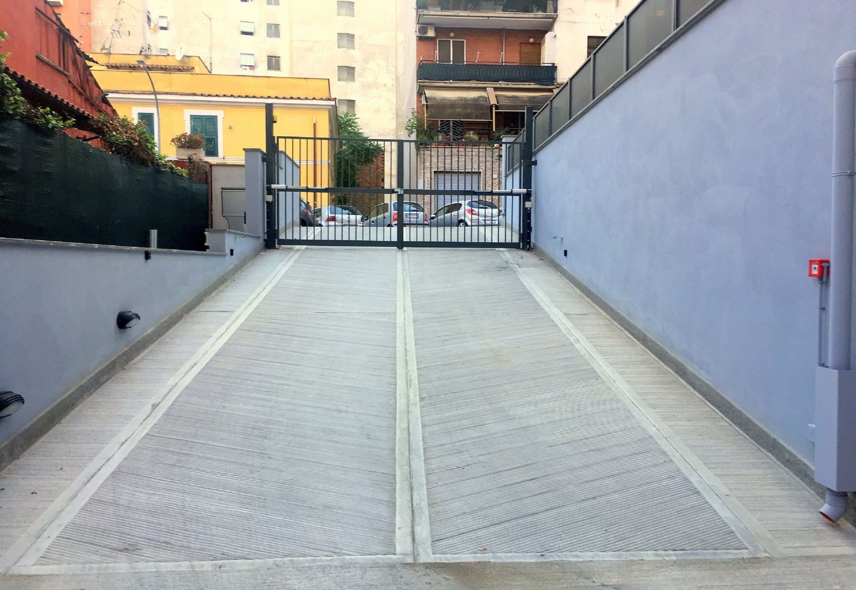 A gated parking area with a metal gate and a concrete ramp leading to a building entrance.