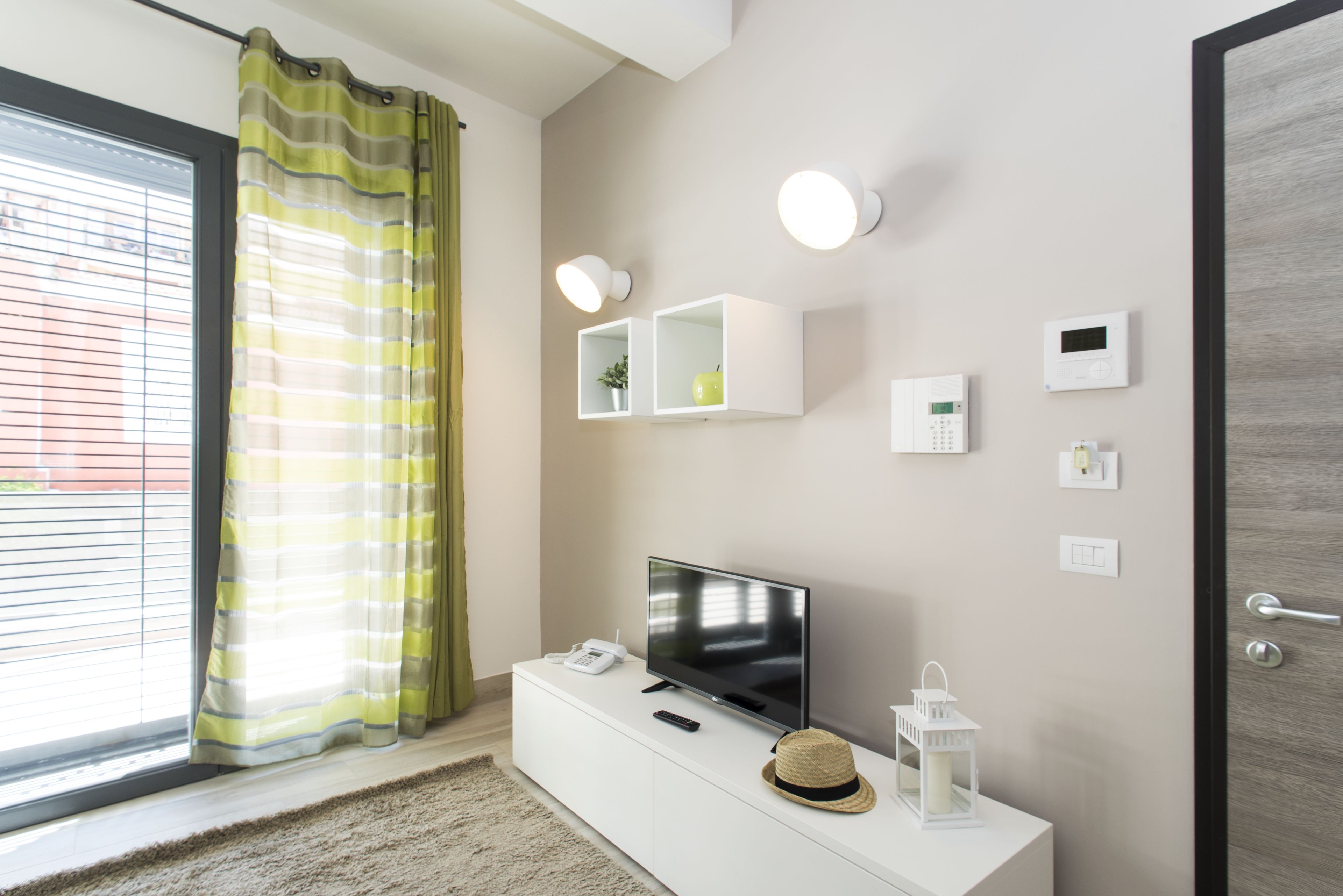 A modern living room with a flat-screen TV, a white console, a remote, a telephone, and decorative items.