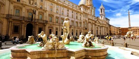 A historic fountain with multiple statues in a public square, surrounded by classical architecture.