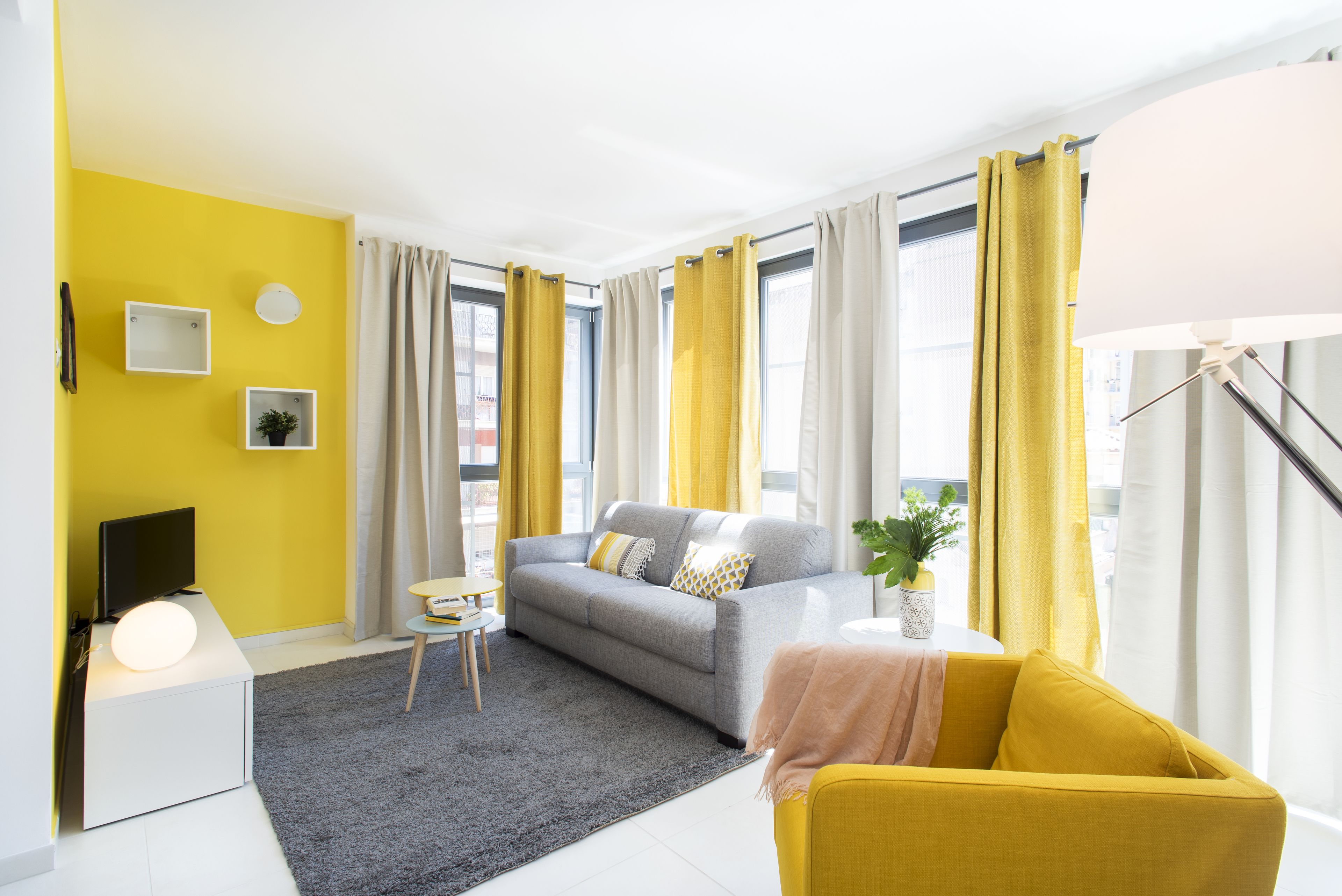 A modern living room with a grey sofa, yellow and white curtains, a small side table, and a yellow armchair.
