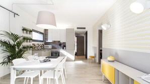 Una cocina moderna con armarios blancos, una zona de comedor con sillas blancas y una pared de acento amarilla.