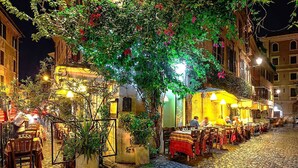 Calle adoquinada bordeada de mesas al aire libre en un restaurante, rodeada de edificios con iluminación cálida.