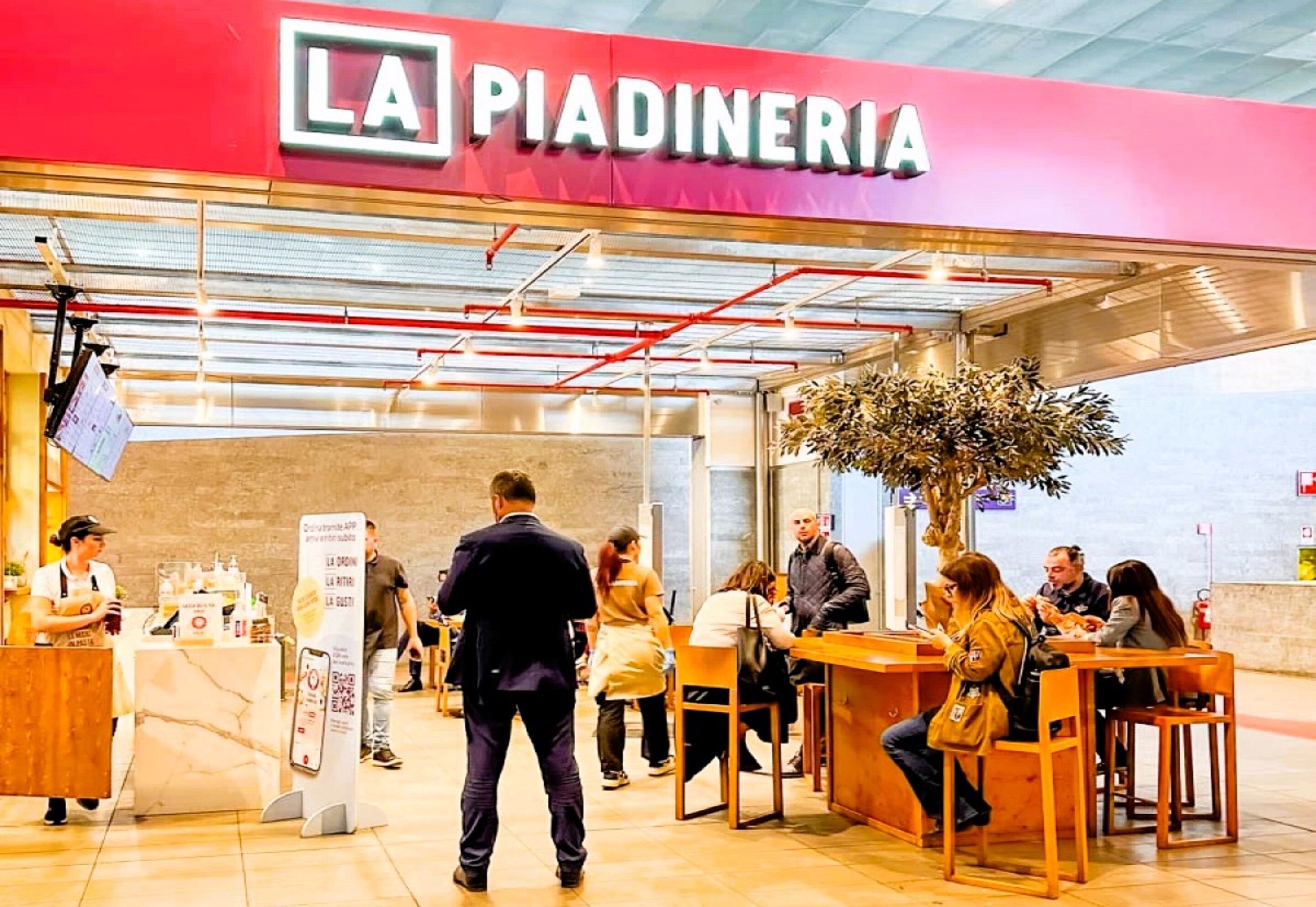 A restaurant named "LA PIADINERIA" with a modern interior, seating area, and a counter where staff are serving.