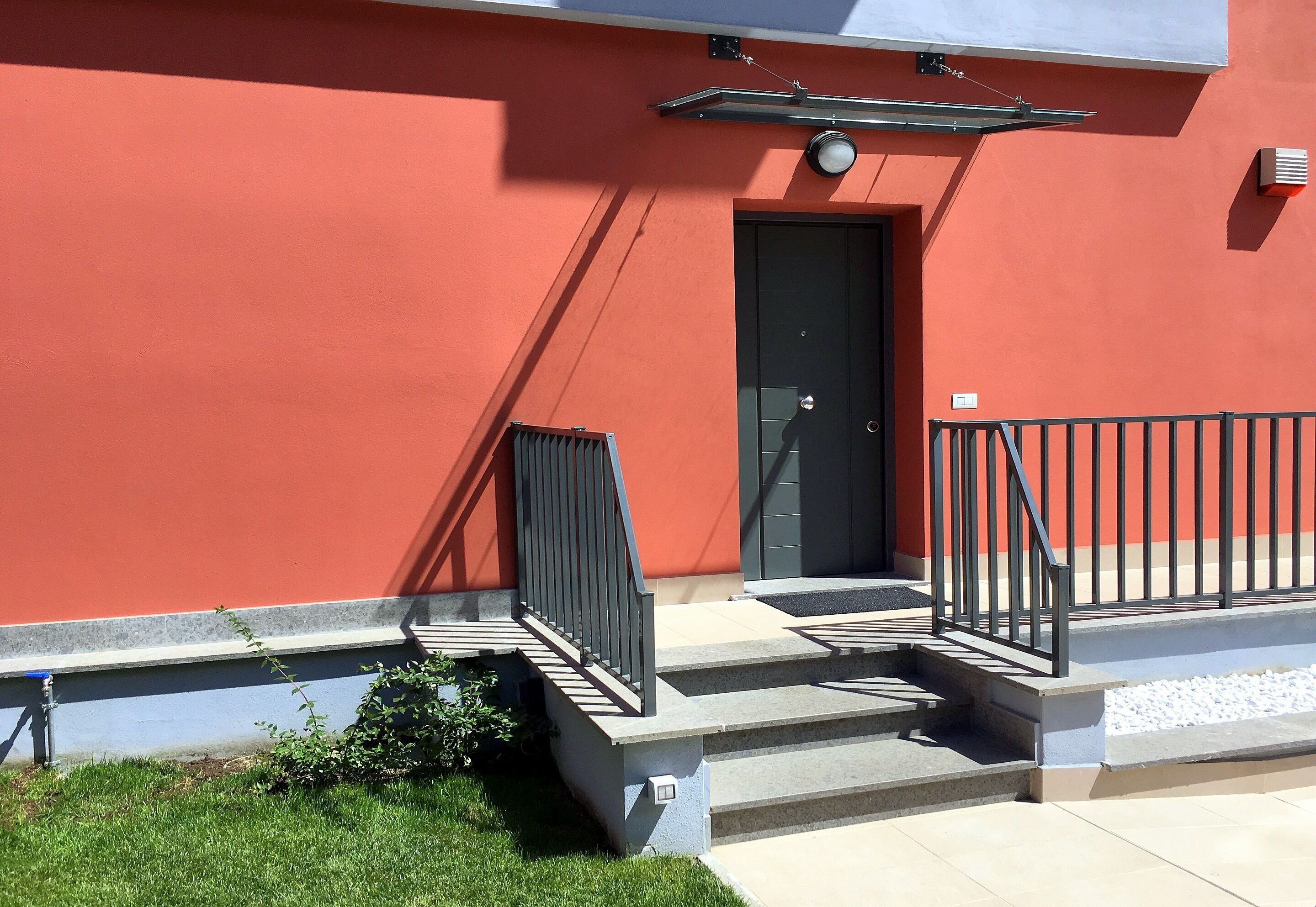 Un bâtiment à la façade rouge, avec une porte noire et une rambarde noire sur les marches menant à l’entrée.