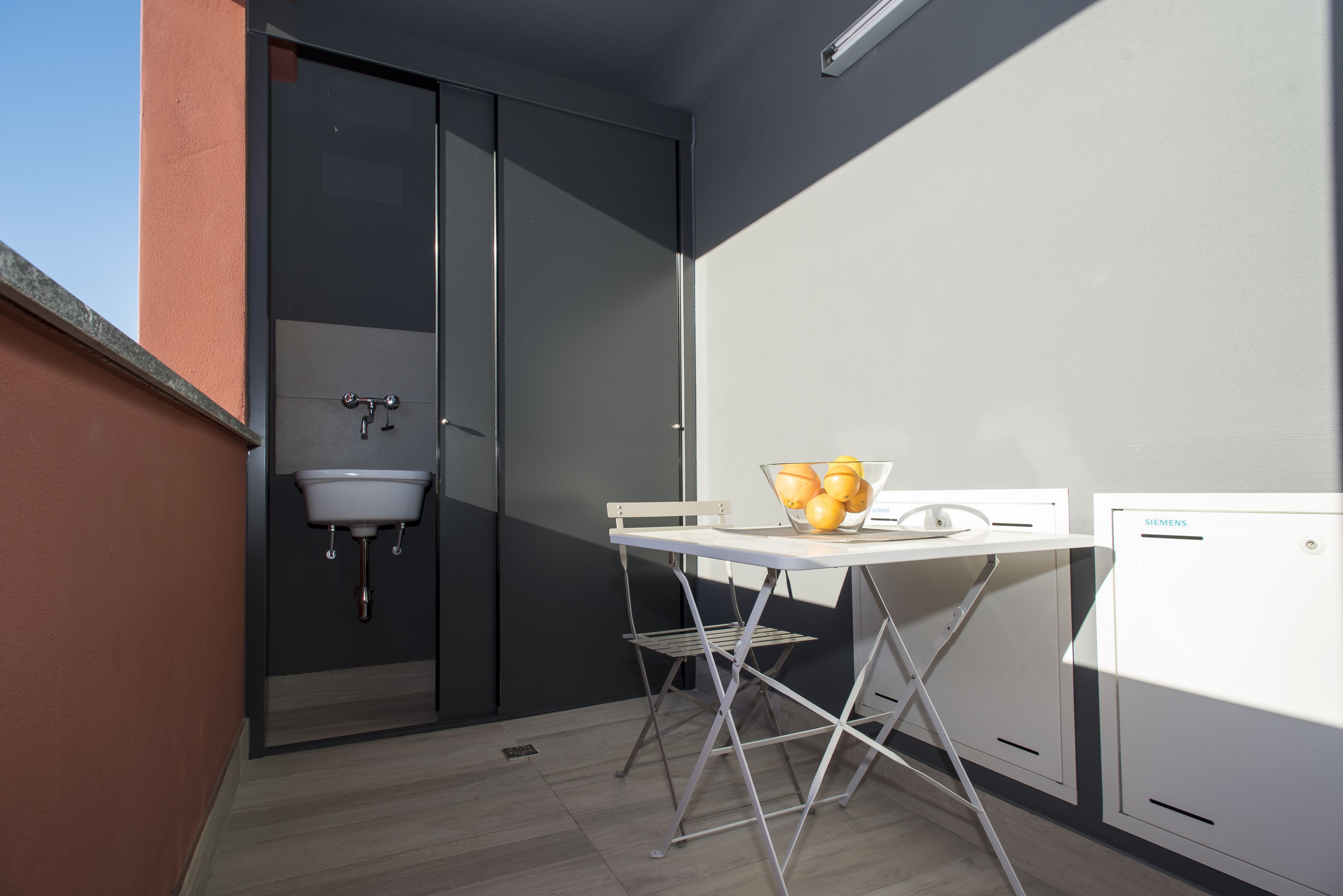 A compact balcony with a white table, a bowl of fruit, a Siemens refrigerator, and a sink.