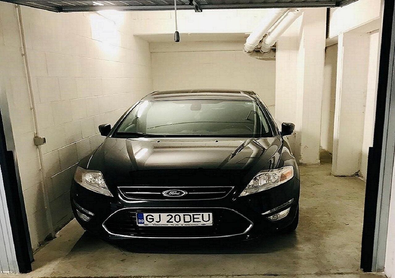 Un coche negro estacionado en un estacionamiento estrecho con paredes blancas y suelo de hormigón.