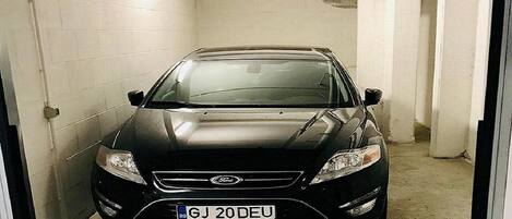 Un coche negro estacionado en un estacionamiento estrecho con paredes blancas y suelo de hormigón.