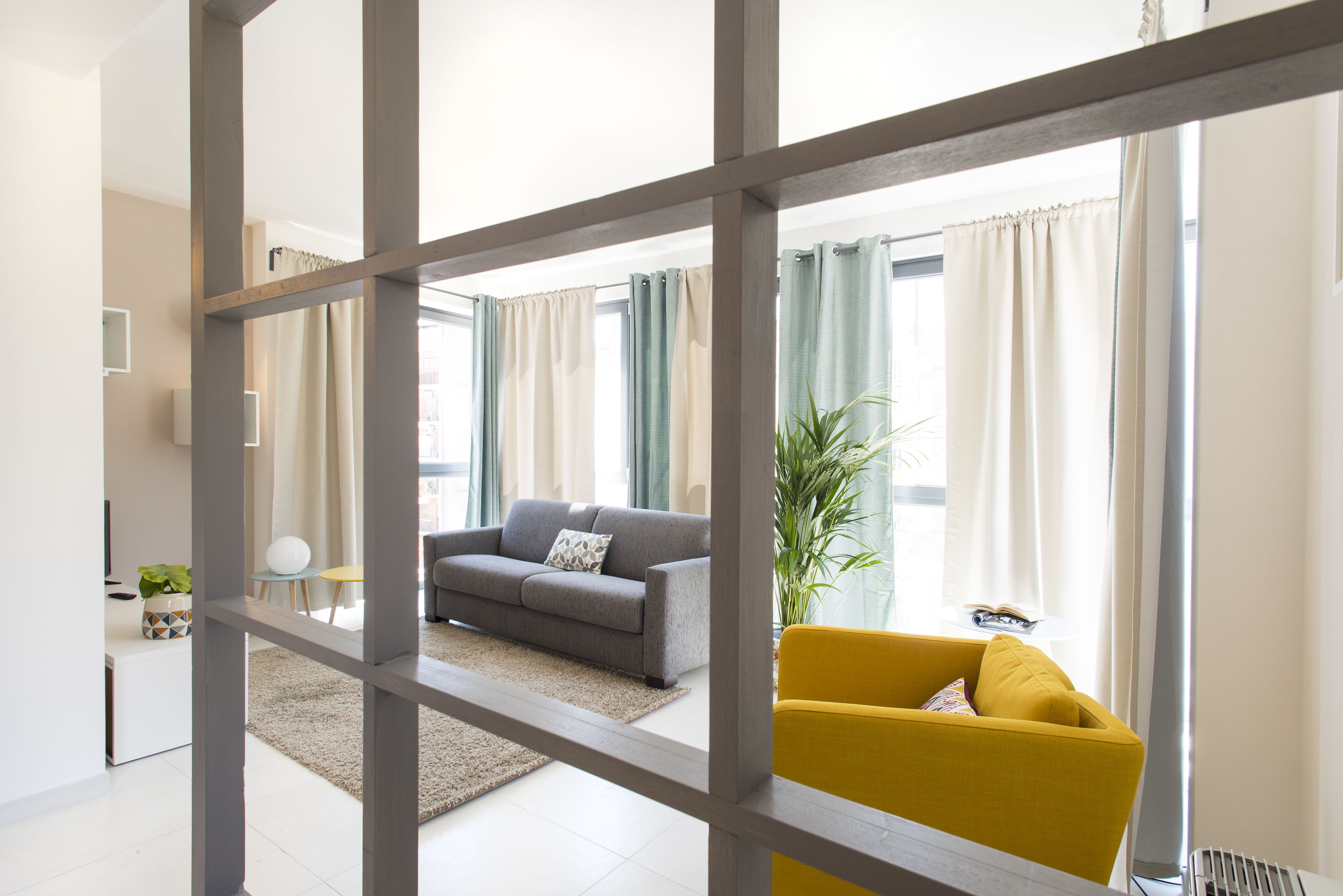 Una sala de estar moderna con un sofá gris, un sillón amarillo y una pequeña mesa con una planta.