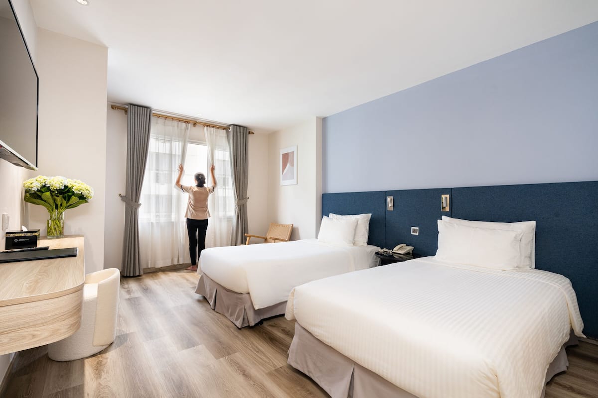 Hotellihuone, jossa on kaksi sänkyä, työpöytä, tuoli, televisio ja ikkuna, jossa on verhot.