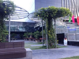 Un espacio exterior con un edificio moderno, un banco de madera y una escultura.