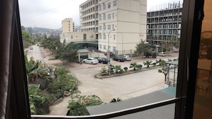 A view from a window overlooking a street with buildings, parked cars, and a small garden area. - Kocmoc Ha Long (Ha Long)