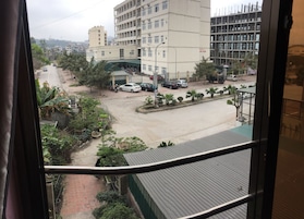 Vista desde una ventana que da a una calle con edificios, coches estacionados y una pequeña zona ajardinada.