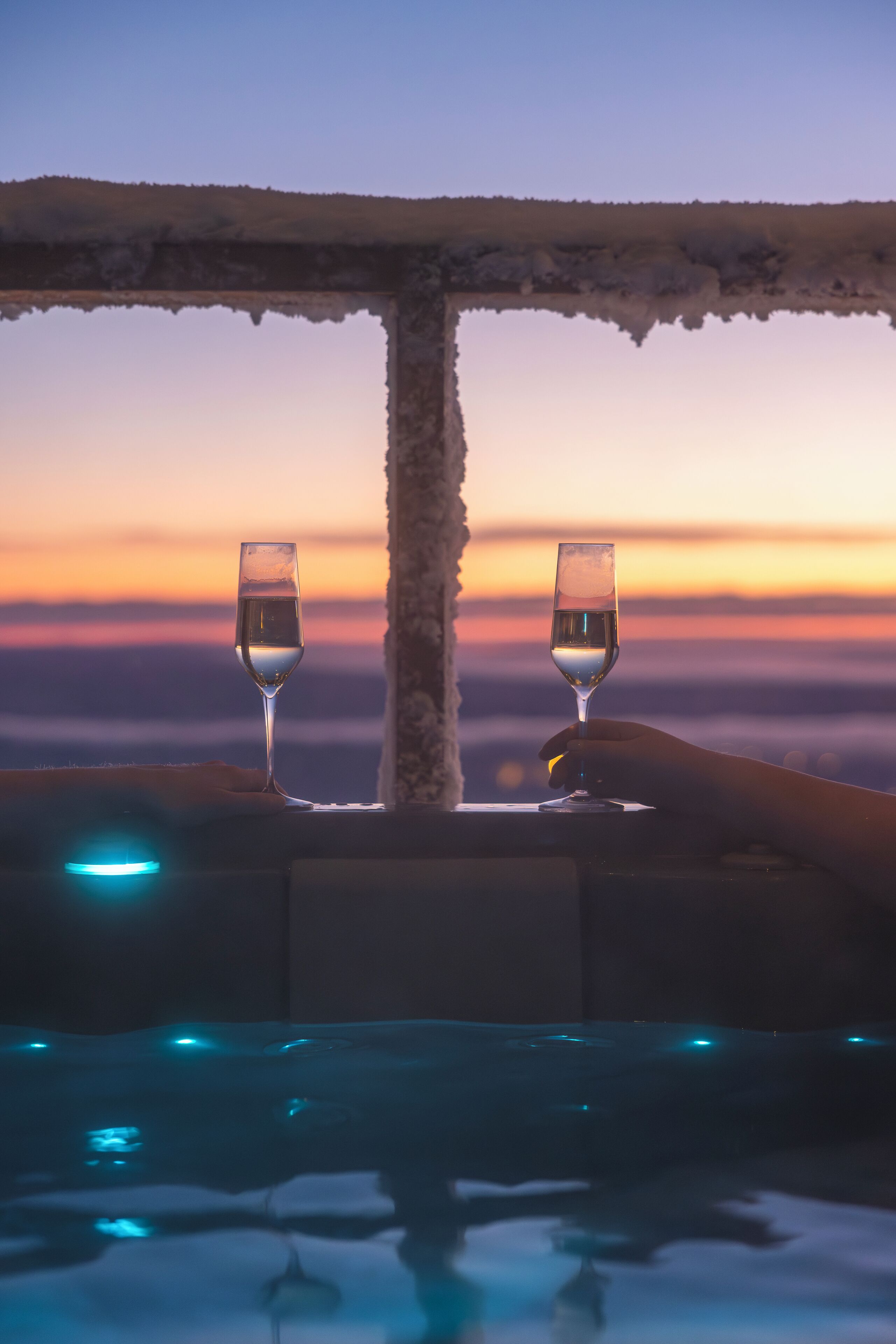 Dos vasos de agua sobre una mesa con vista a un atardecer.