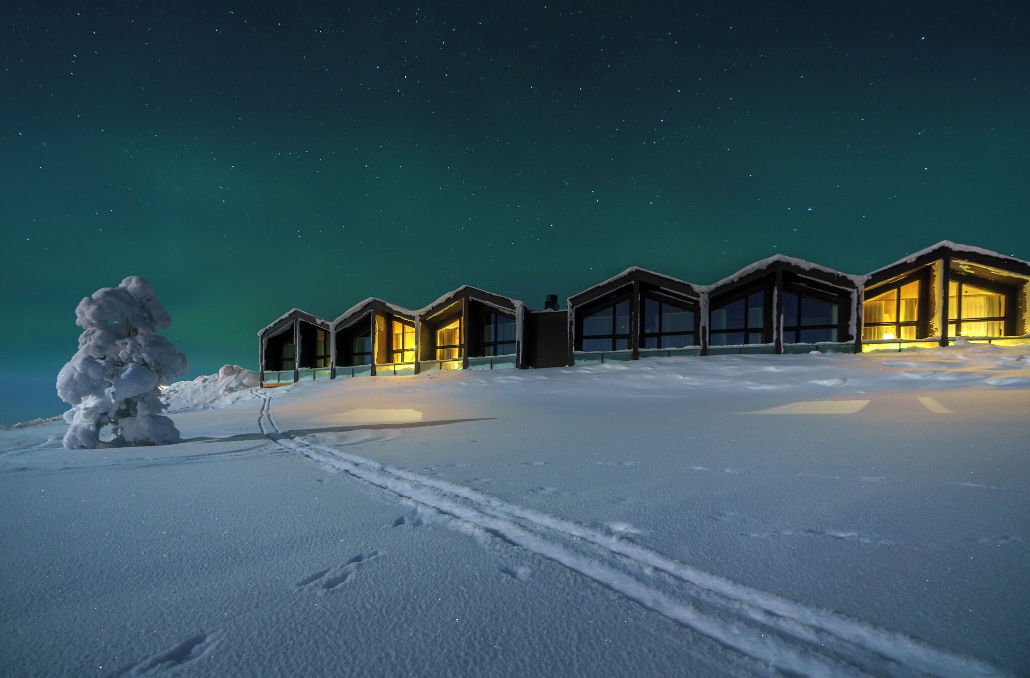 A row of snow-covered cabins with illuminated windows against a starry night sky.
