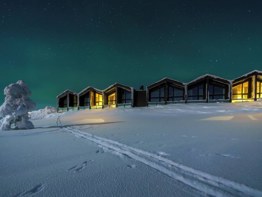 A row of snow-covered cabins with illuminated windows against a starry night sky.