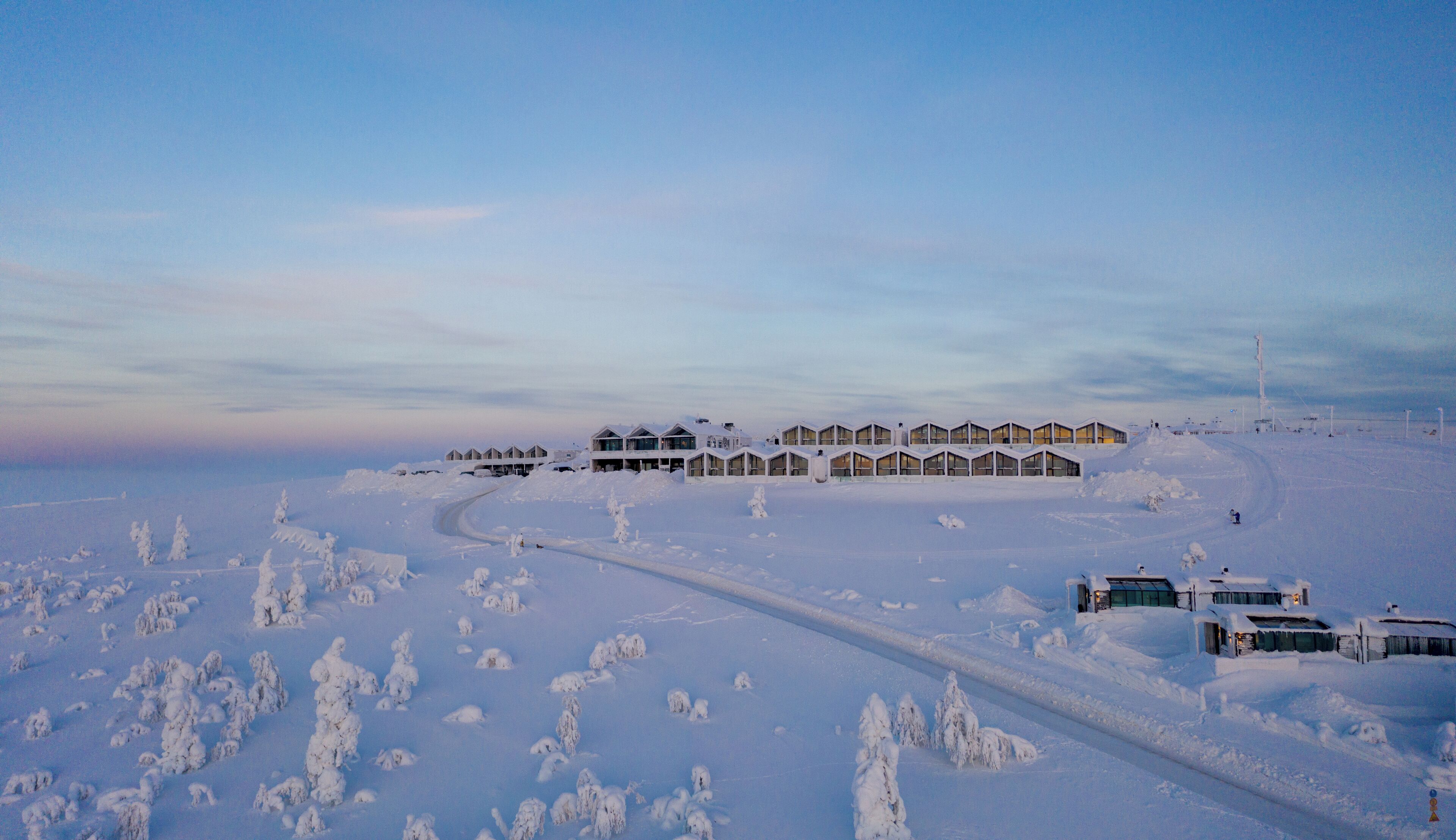 Un paysage enneigé, avec une rangée de bâtiments modernes à plusieurs étages dotés de grandes fenêtres, qui semblent être un hôtel ou un complexe touristique.