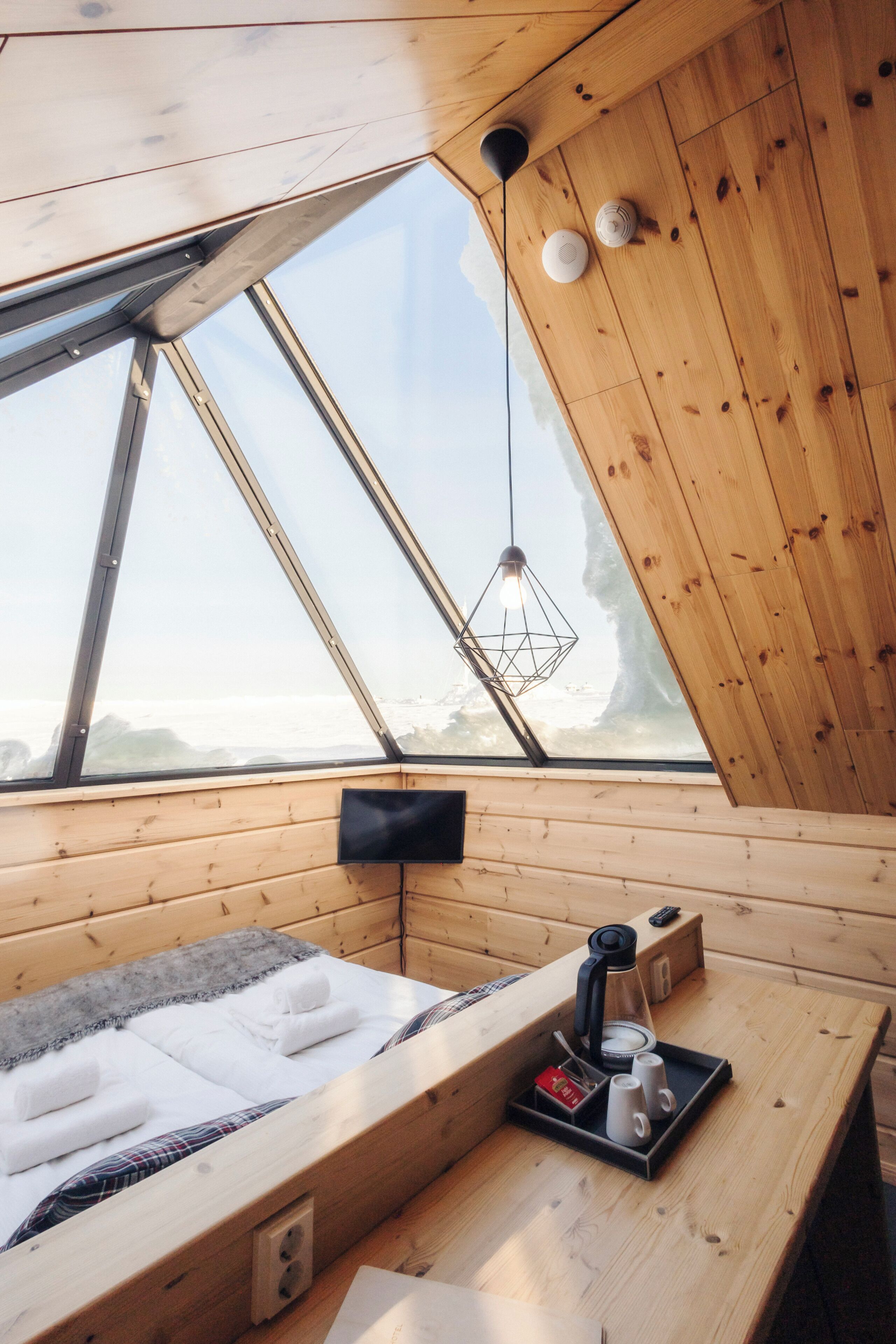 A wooden cabin with a bed, a table with a coffee maker, and a view through a skylight.