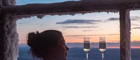 Une personne dans un bain à remous, avec deux verres d’eau, une fenêtre donnant sur le ciel et les montagnes.