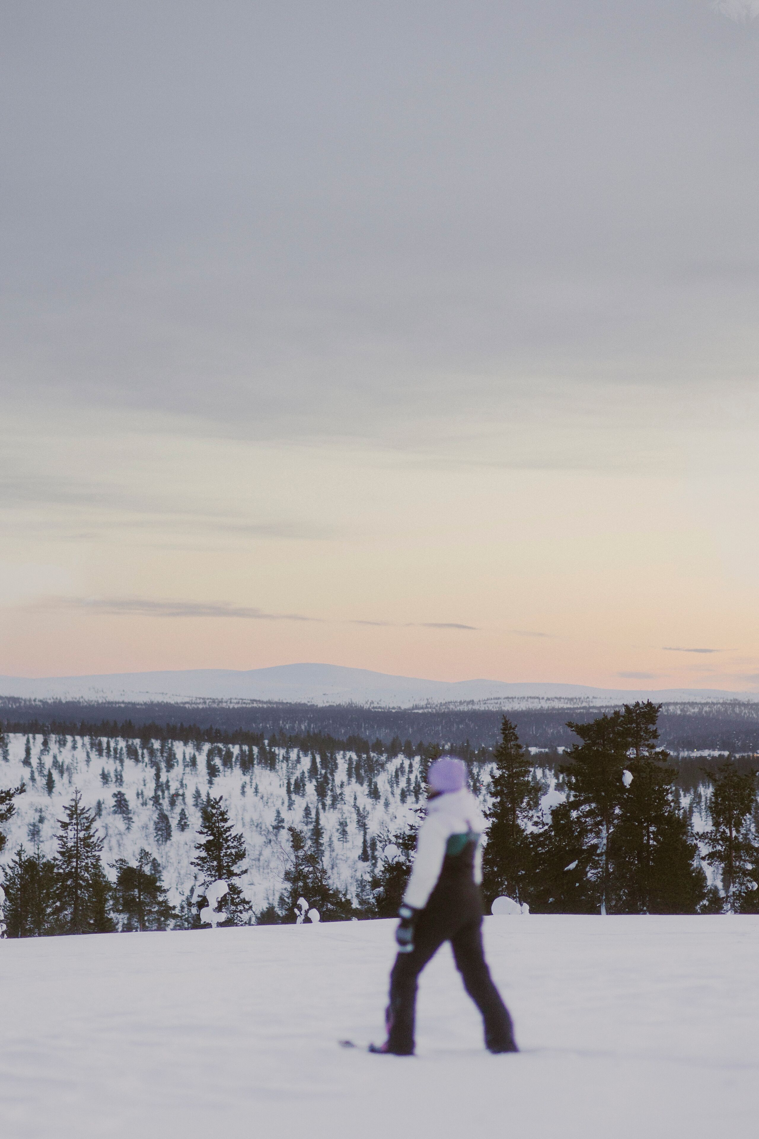 A person walking on a snow-covered path with a forest and mountains in the background.