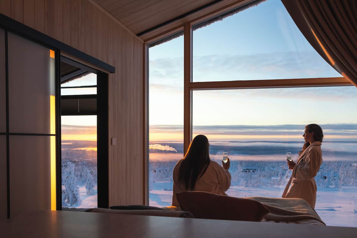 A room with a large window overlooking a snowy landscape, a bed, and a wooden wall.