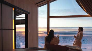 A room with a large window overlooking a snowy landscape, a bed, and a wooden wall.