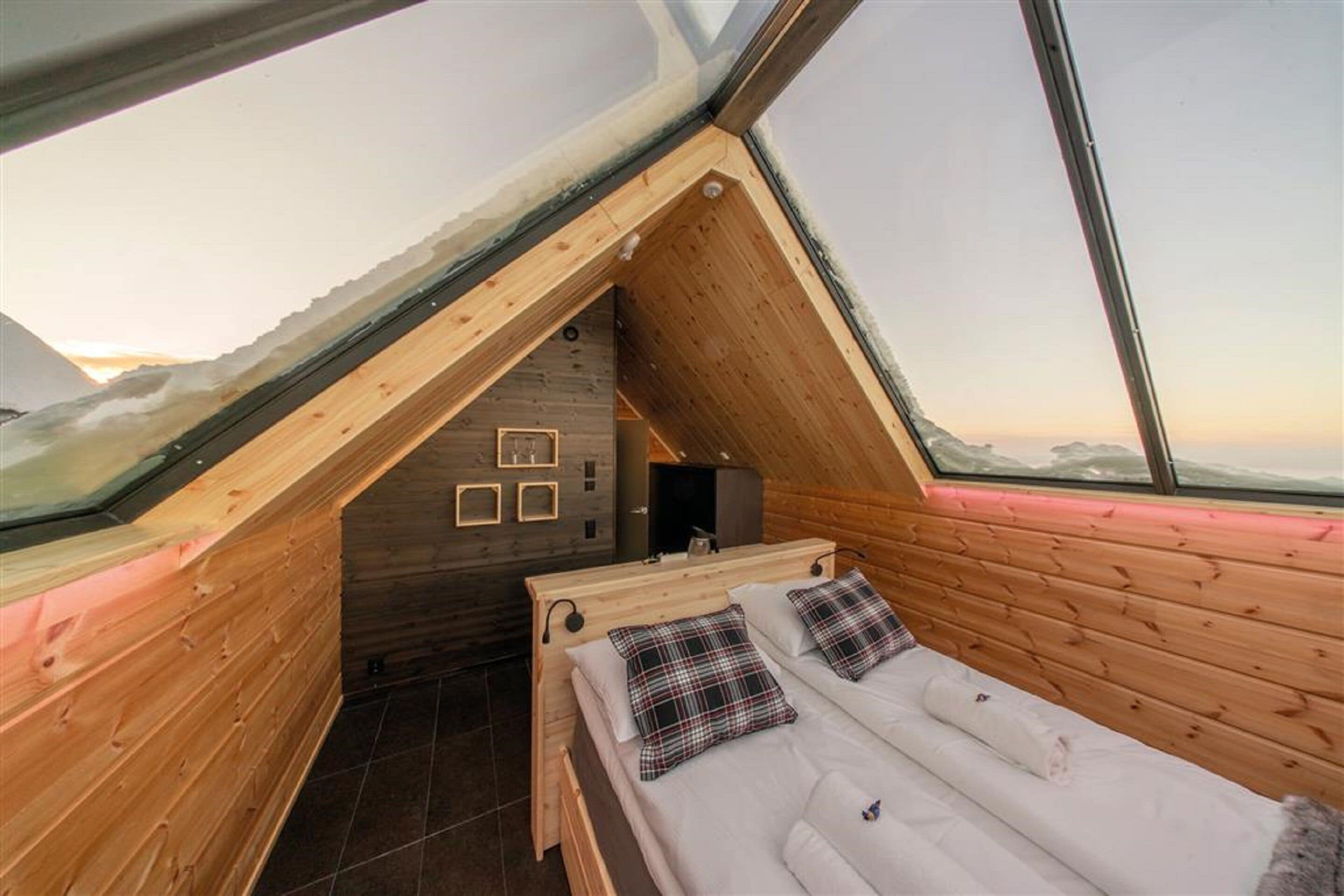 Um quarto de sótão acolhedor, com teto inclinado, paredes de madeira e uma cama com almofadas xadrez.