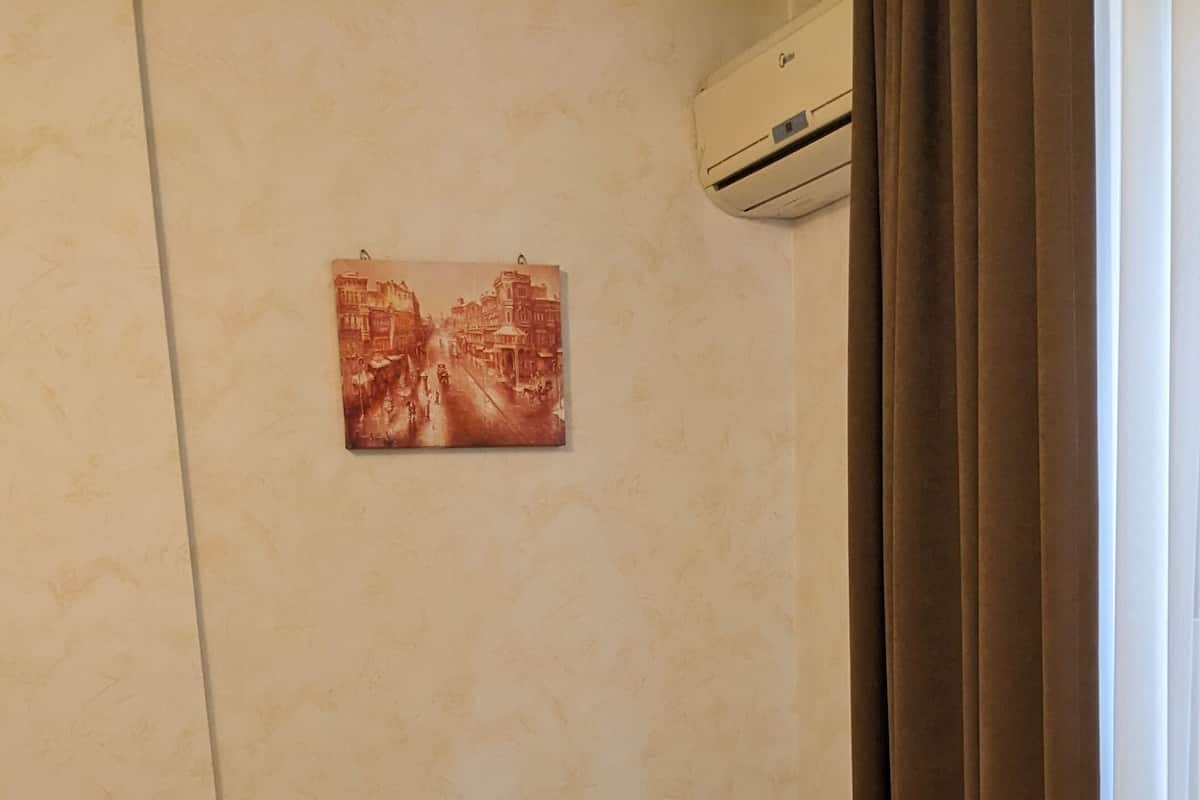 Una cama bien hecha con cabecera de madera, una mesita de noche con cajones, un equipo de aire acondicionado en la pared y un cuadro sobre la cama.