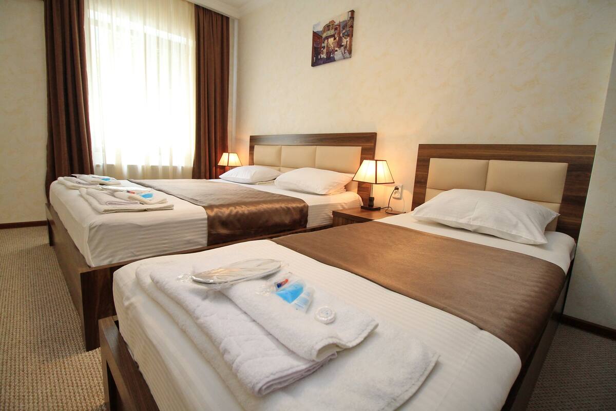 Habitación de hotel con dos camas, cada una con cabecera, mesitas de noche con lámparas y toallas sobre las camas.