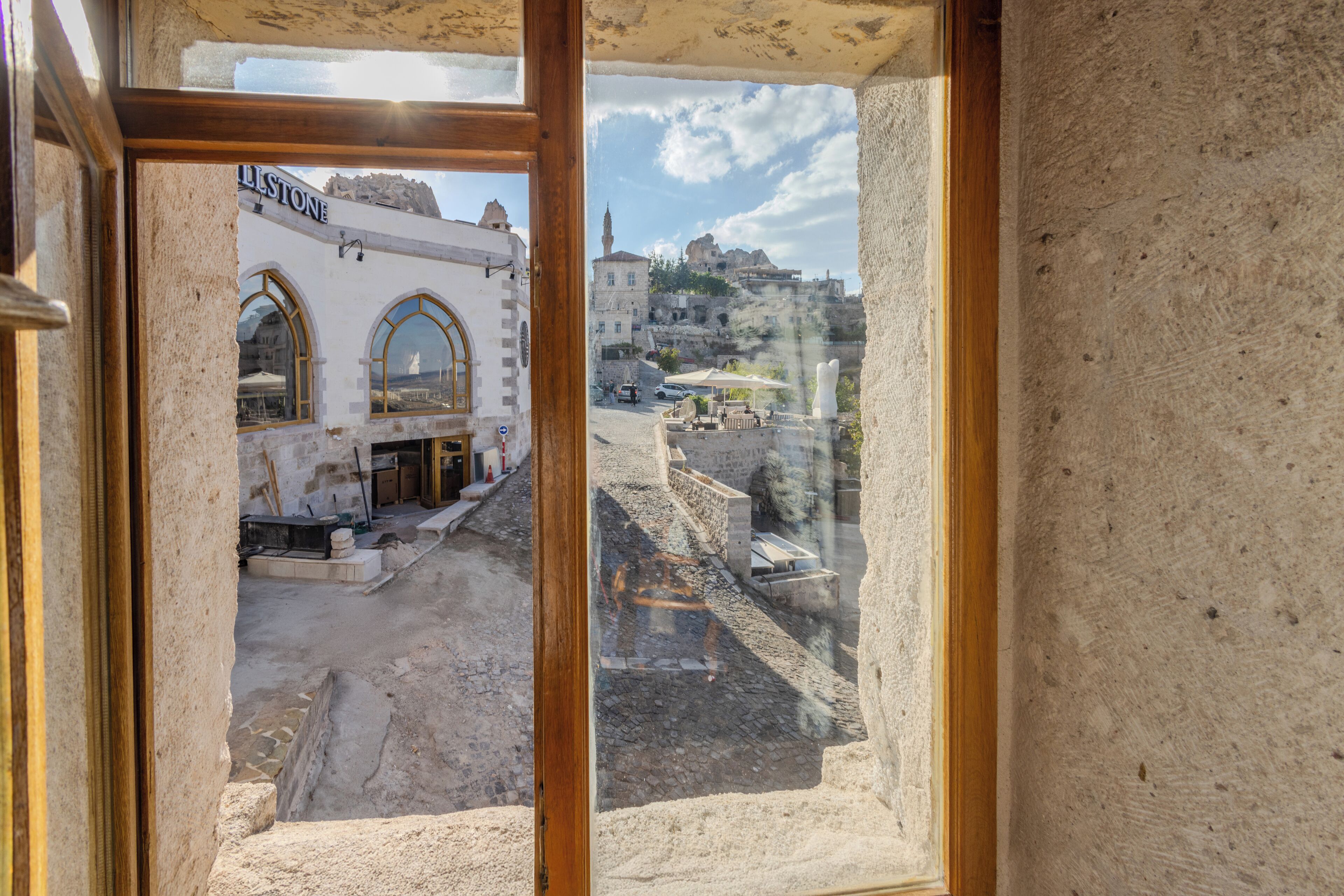 A view through a window of a building with a stone facade, a sign reading "ILLSTONE," and a street scene with buildings and a mosque in the background.