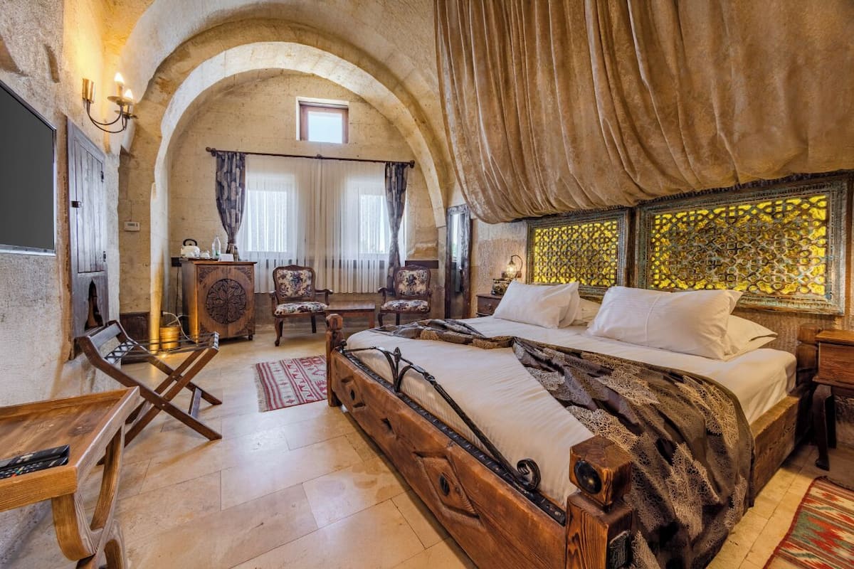 A rustic bedroom with a wooden bed, arched ceiling, and a view of a yellow patterned wall.