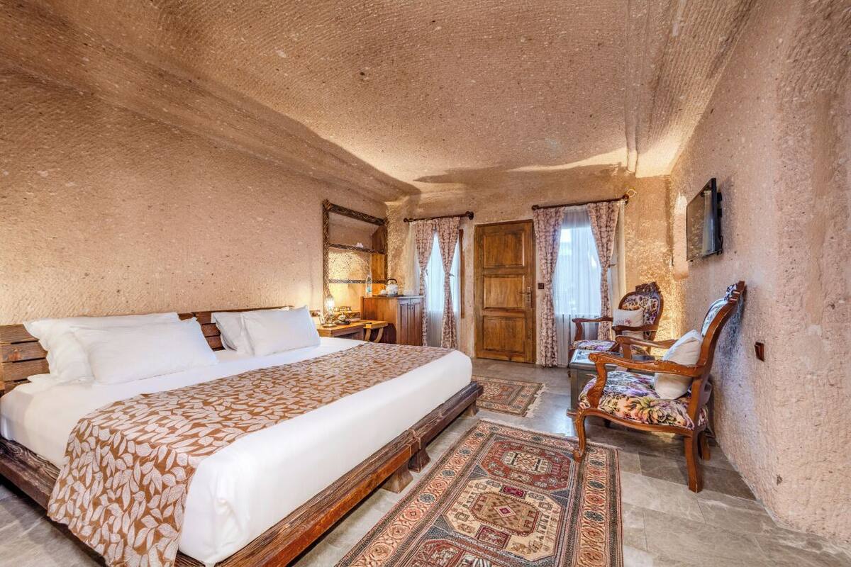 A bedroom with a large bed, wooden headboard, a desk, a chair, and a patterned rug.