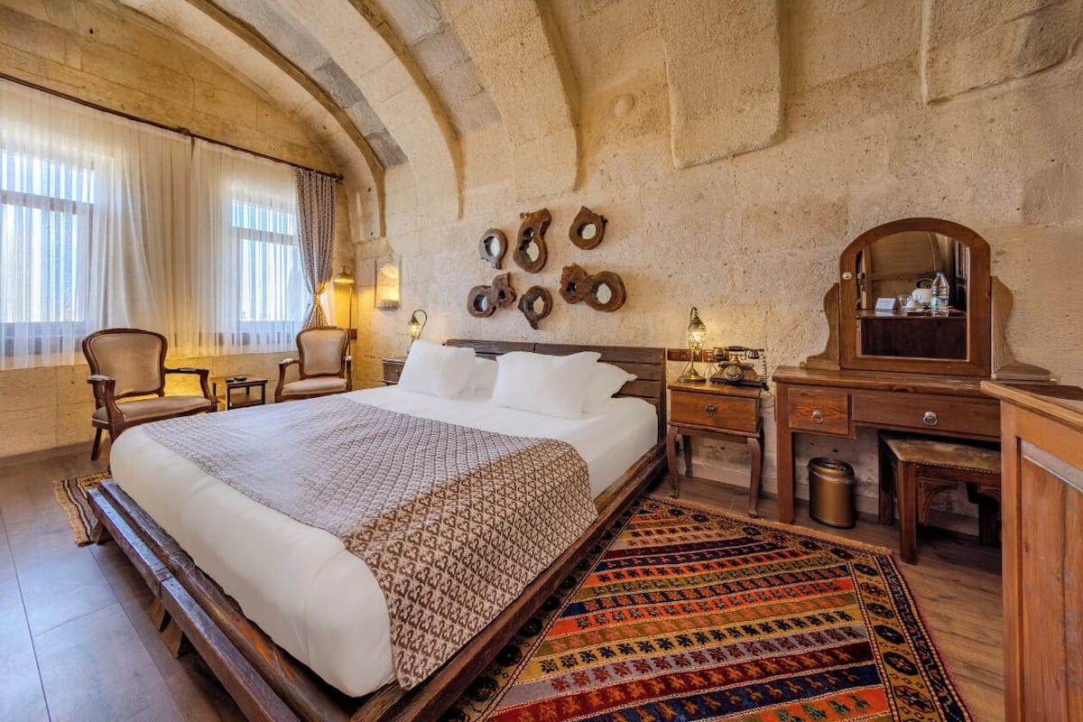 A spacious bedroom with a large bed, a wooden dresser, a desk, and a mirror.