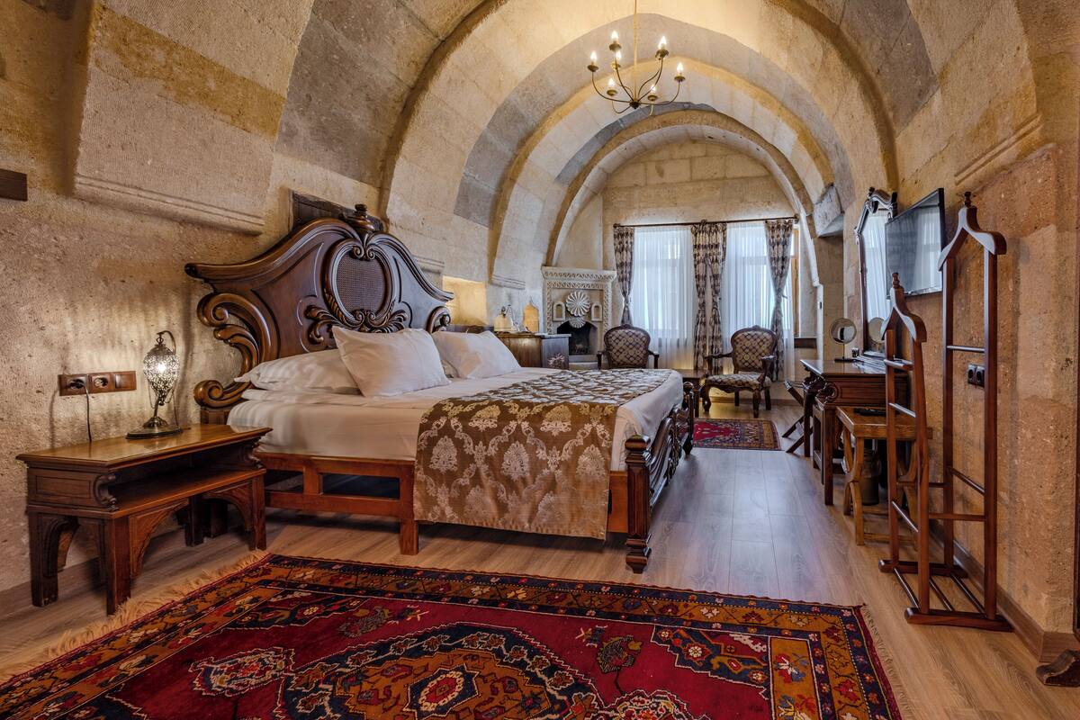 A traditional bedroom with a large bed, wooden furniture, and a red patterned rug.