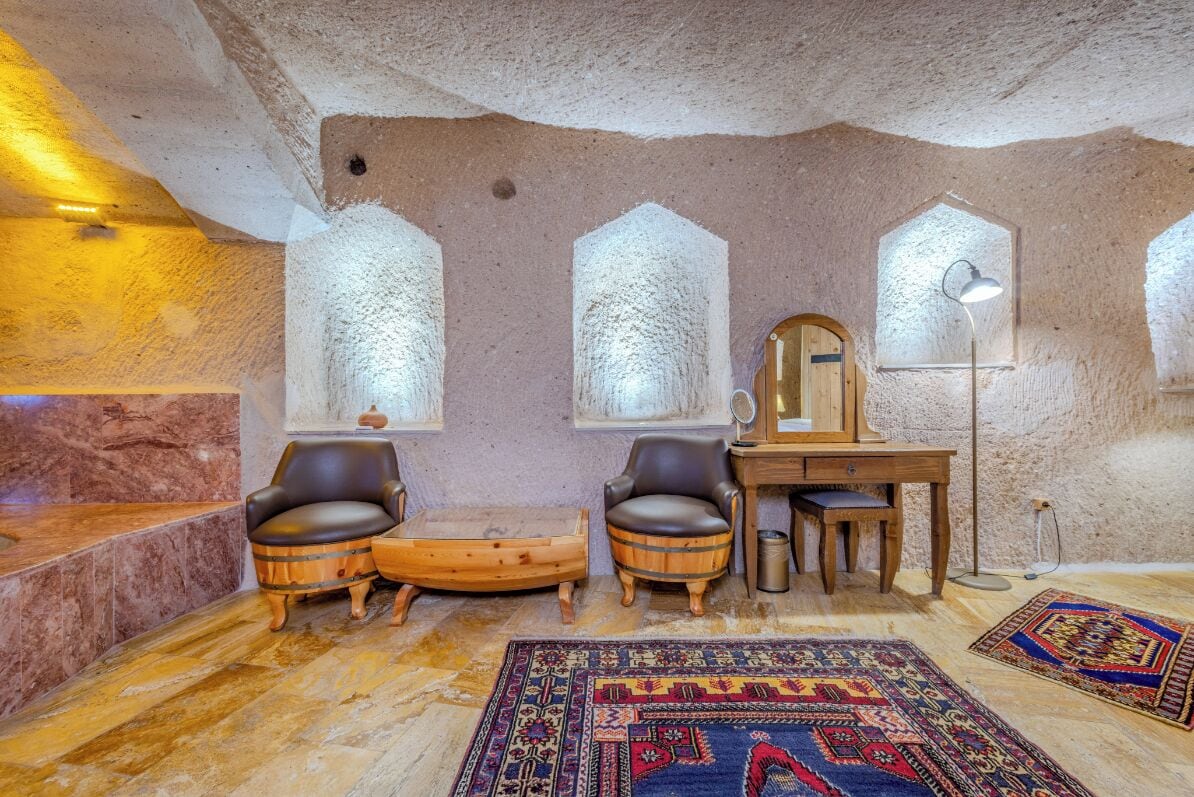 Una habitación acogedora con pared de piedra, dos sillones de cuero, un escritorio de madera, una alfombra y una lámpara.