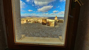 Une vue à travers une fenêtre donnant sur une cour pavée, une porte en bois et un mur de pierre.