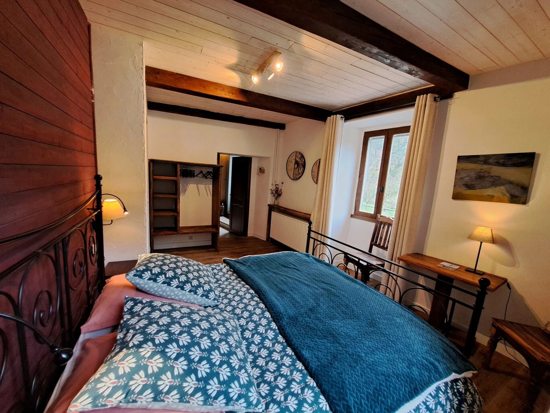 A bedroom with a bed, a wooden headboard, a desk, and a window with curtains.