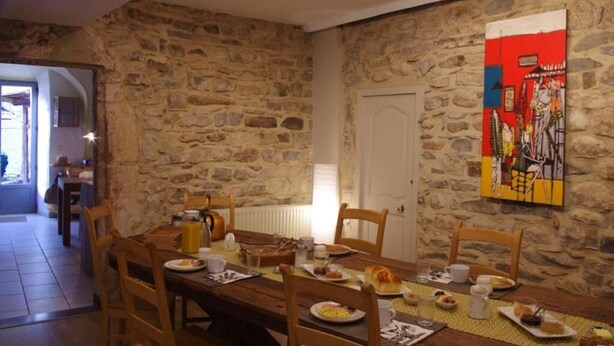 A dining area with a stone wall, wooden table, chairs, and a painting. - Le Sareymond (Chatillon-en-Diois)