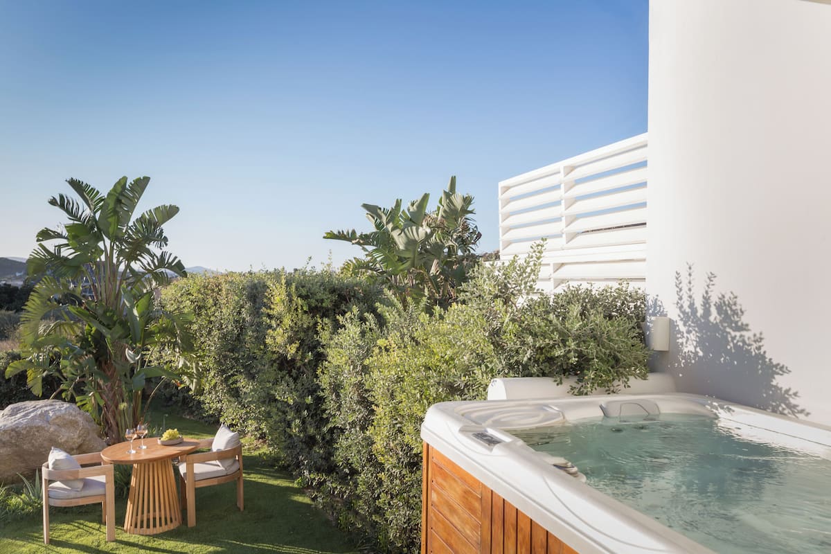 A hot tub with a wooden exterior, surrounded by lush greenery and a clear blue sky.