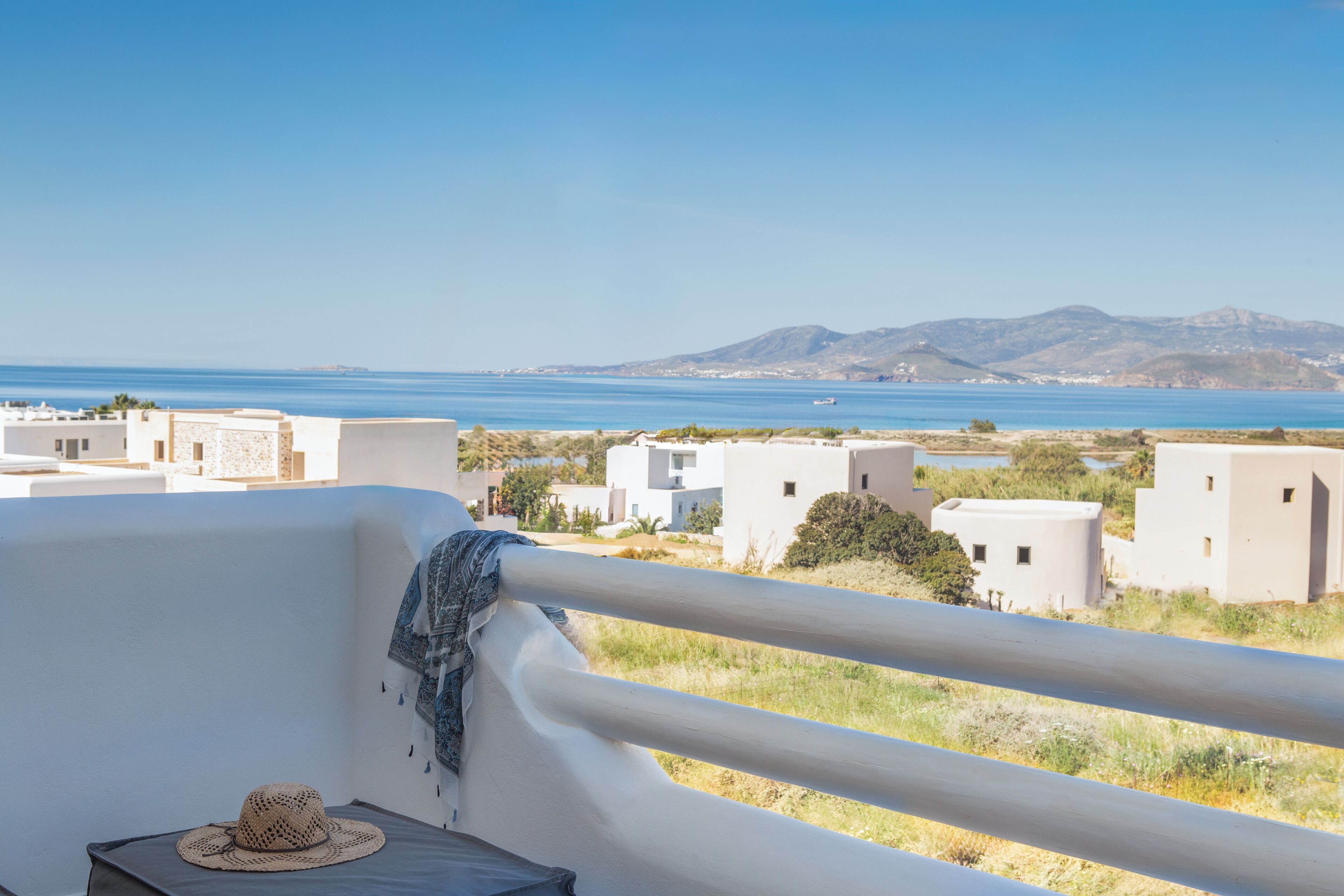 A balcony with a view of a coastal landscape, including buildings and a distant mountain range.