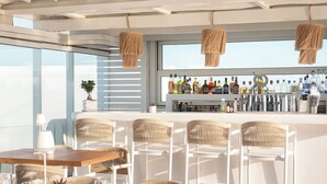 A modern bar area with wicker chairs, a wooden table, and a variety of bottles. - 18 Grapes Hotel (Naxos)