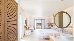 A modern bedroom with a large bed, a round mirror, a white bathroom with a large sink, and a view of the outdoors through a sliding door. - 18 Grapes Hotel (Naxos)
