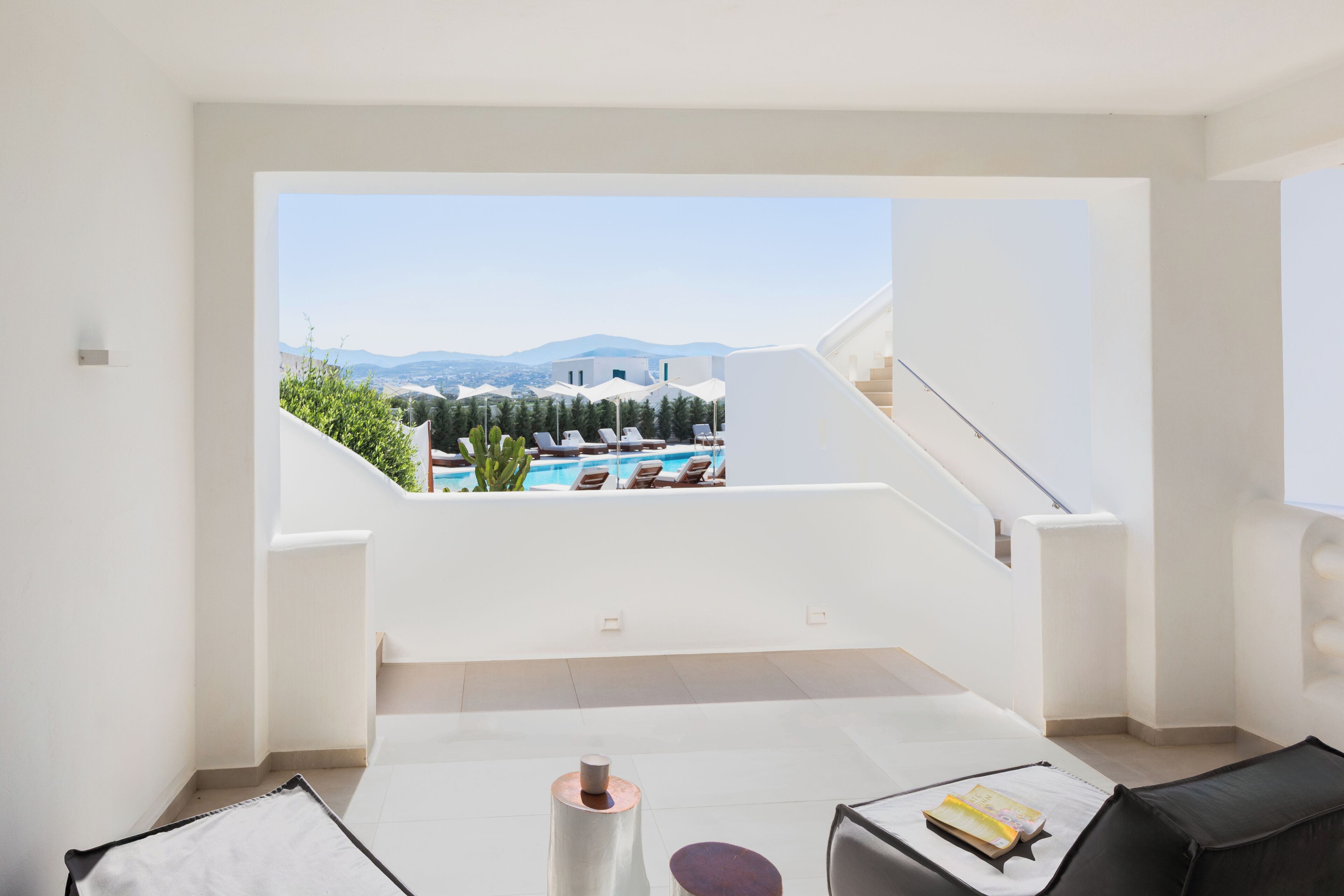 Une chambre moderne avec vue sur une piscine et des montagnes, comprenant un mur blanc, une petite table et une chaise.