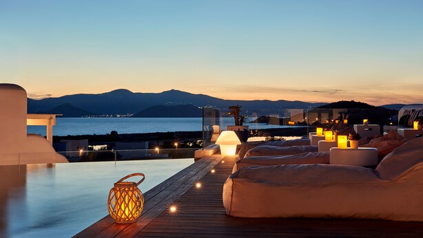 A rooftop terrace with a view of the sea and mountains, featuring a wooden deck, seating area, and ambient lighting. - 18 Grapes Hotel (Naxos)