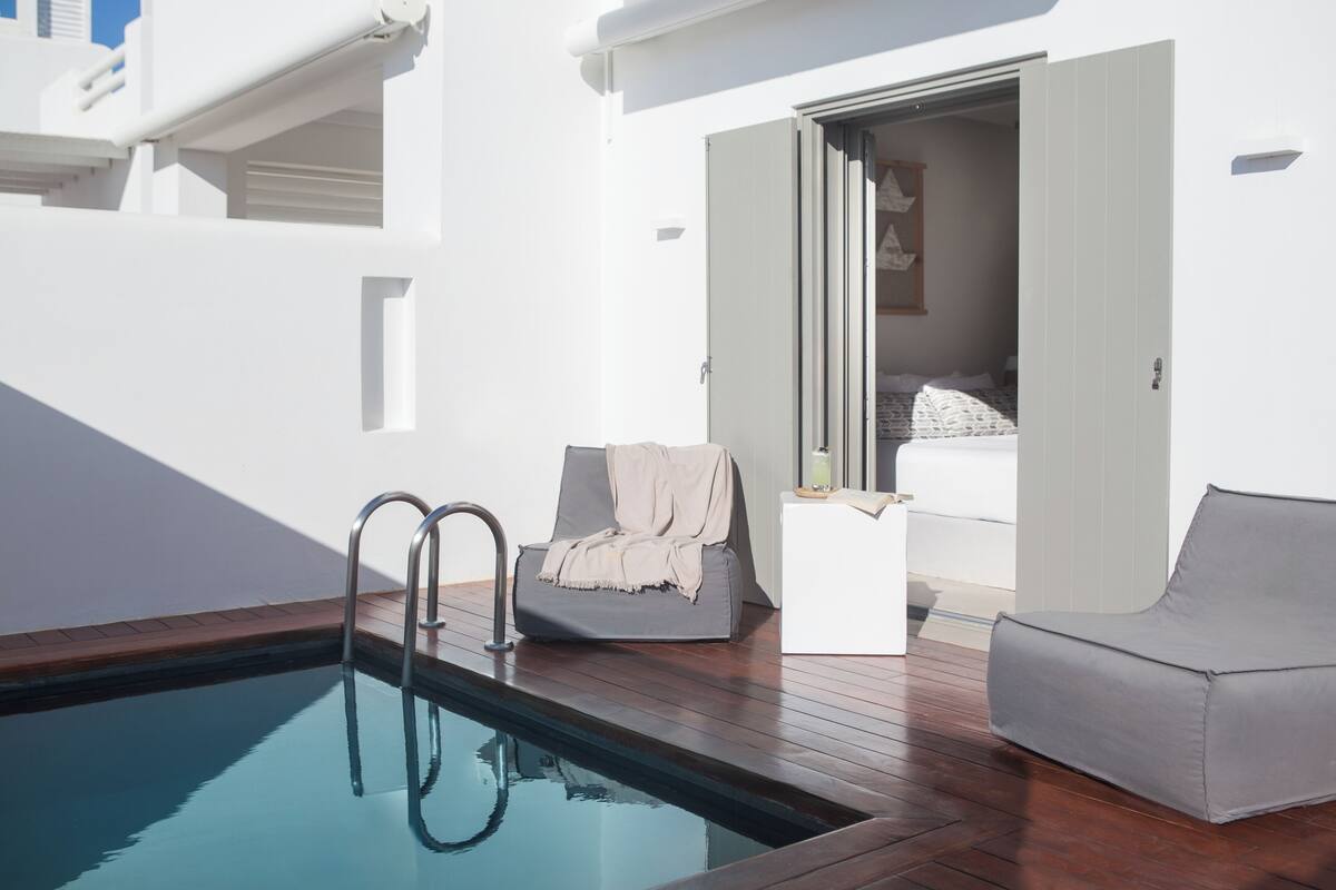A modern indoor pool area with a wooden deck, a gray lounge chair, and a white sofa.