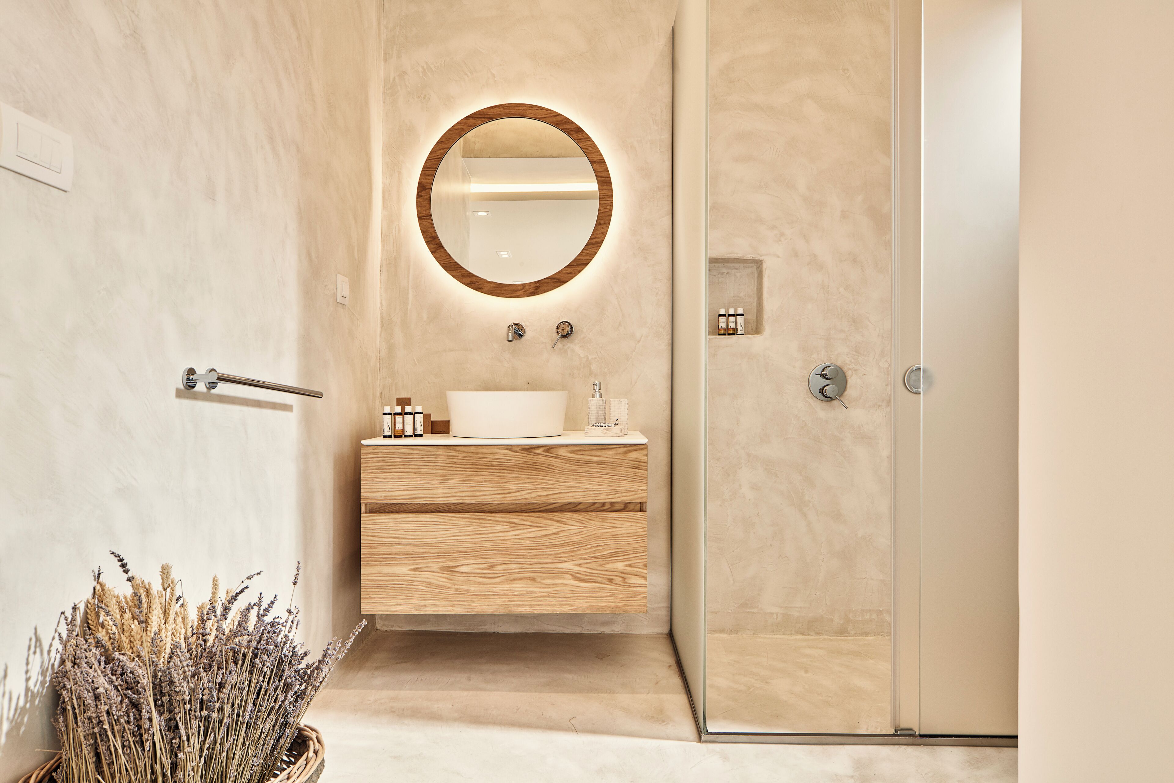 A modern bathroom with a wooden vanity, a round mirror, and a glass shower enclosure.