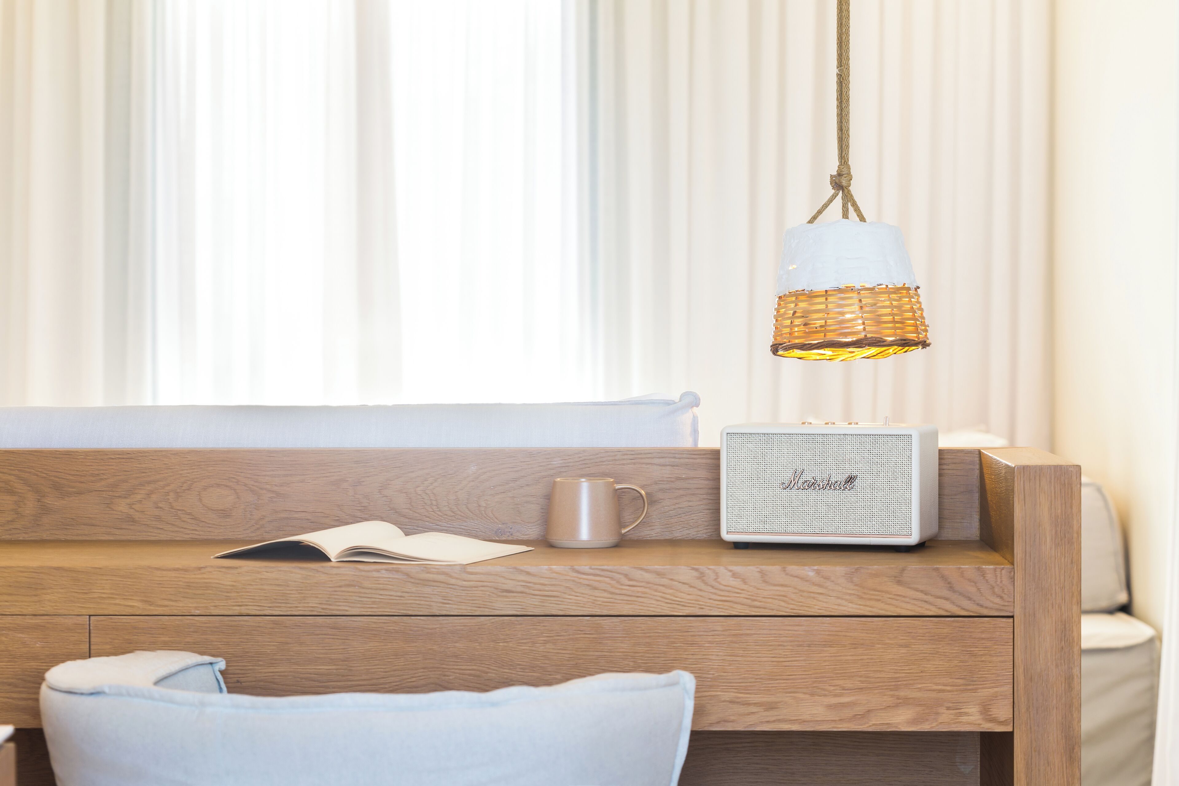 A wooden bedside table with a book, a mug, and a Marshall speaker.