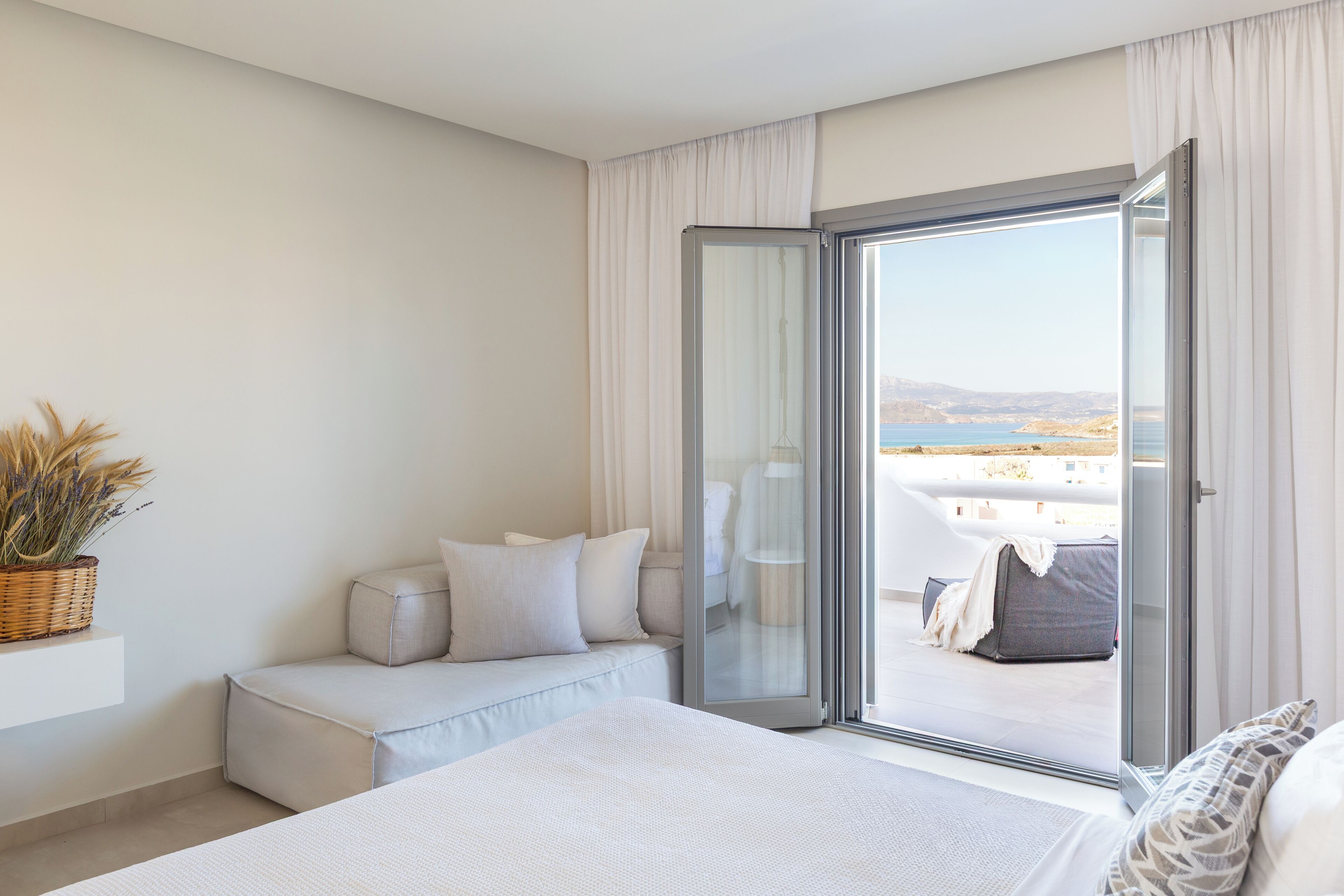 A bedroom with a bed, a seating area with a sofa, a large window, and a view of the outdoors.