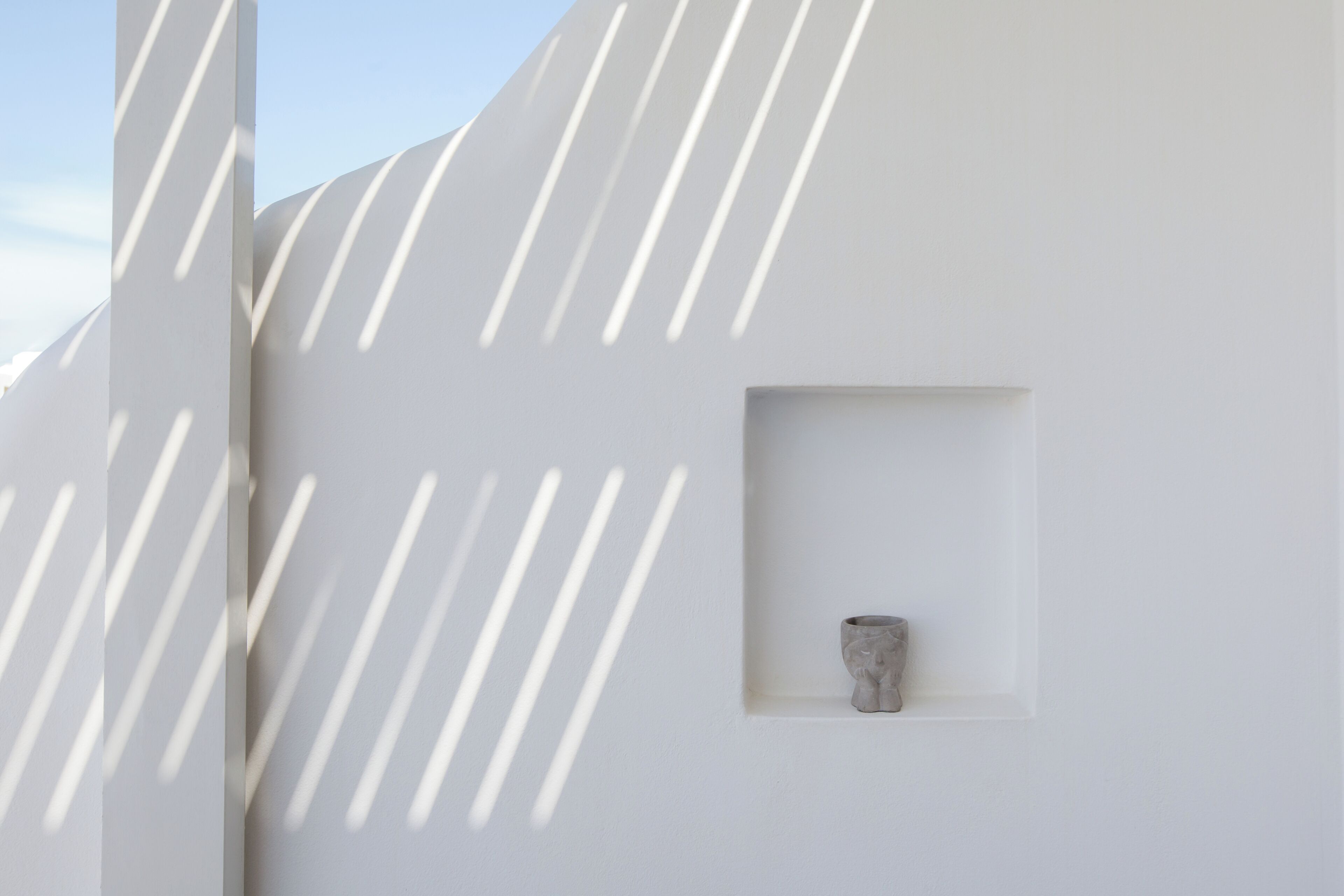 A minimalist interior with a white wall and a small alcove containing a sculpture.