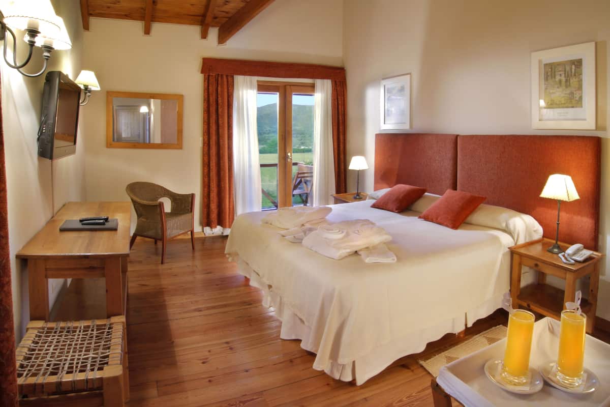 A hotel room with a bed, bedside table, chair, and a view of the outdoors.